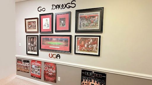 Office wall of framed UGA Bulldogs photos and posters under the words Go Dawgs
