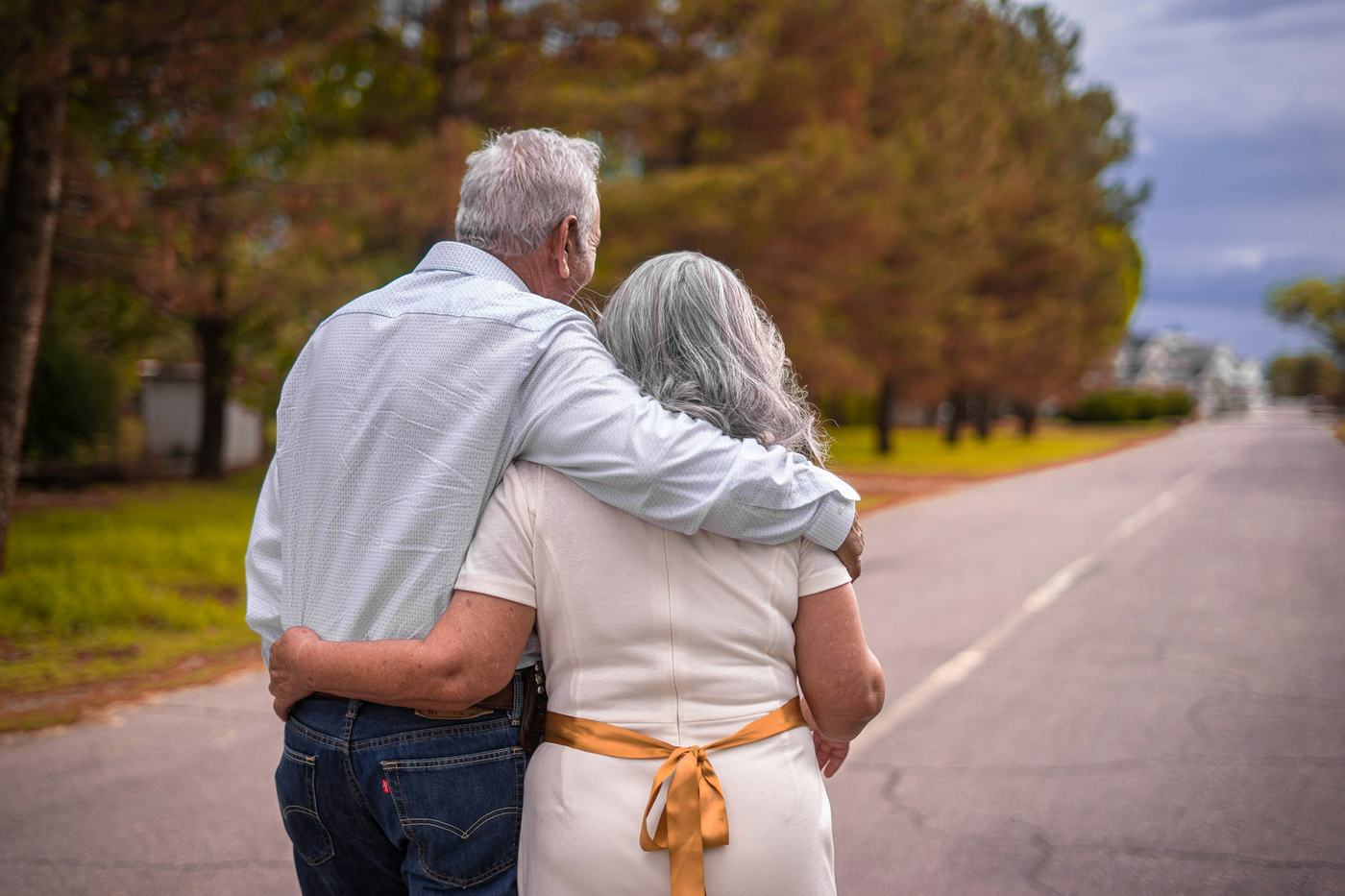 An older couple walking arm in arm down a tree-lined road
