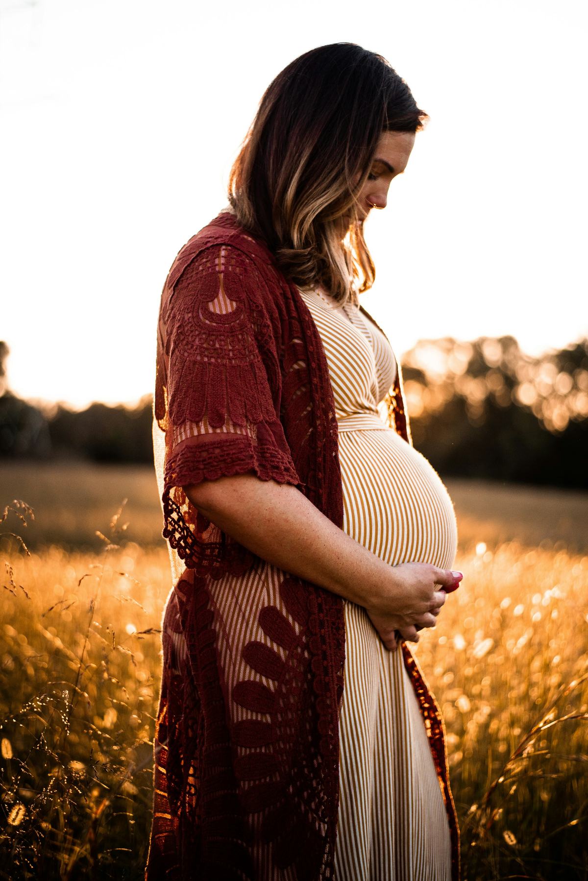 A pregnant woman cradling her belly in a sunlit field